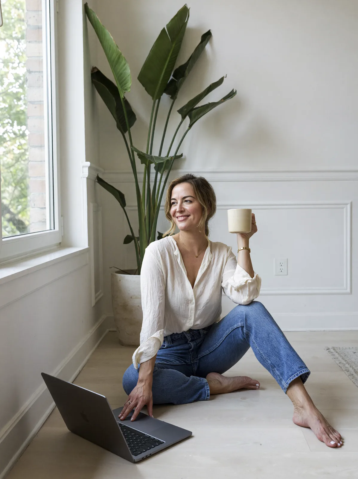 Jessica sitting on the floor with a mug and her laptop